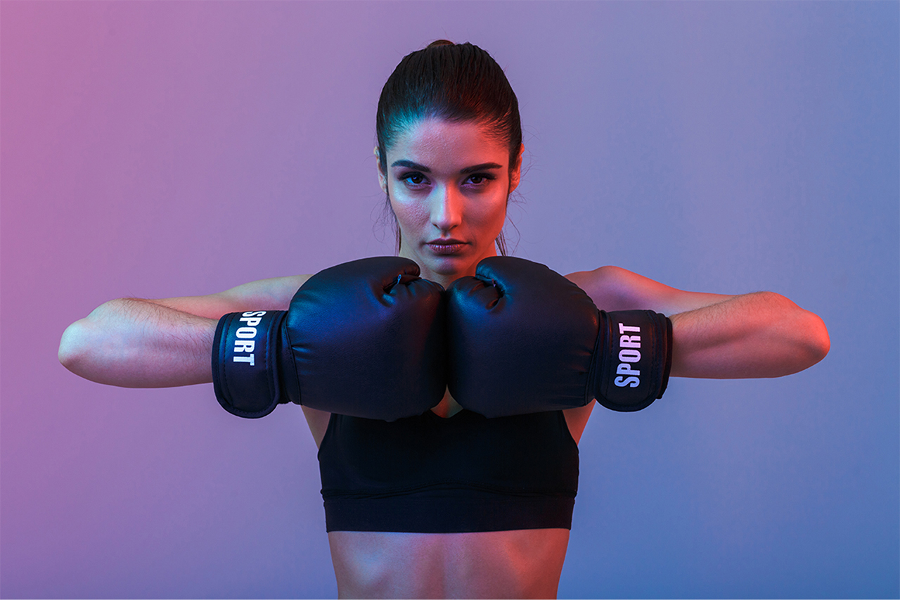 Young woman with boxing gloves, holding fists together. Purple background.