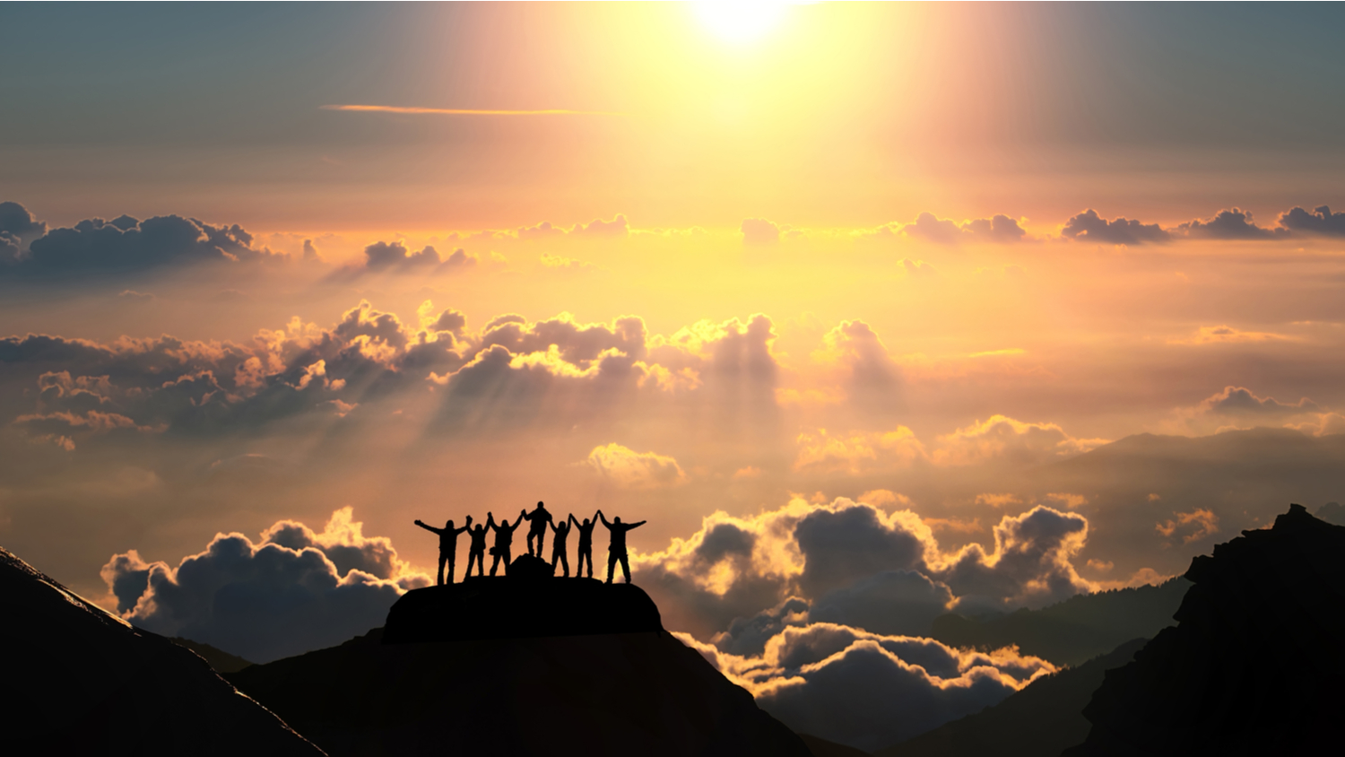 Silhouette of team on a mountain celebrating achievement with sunset background