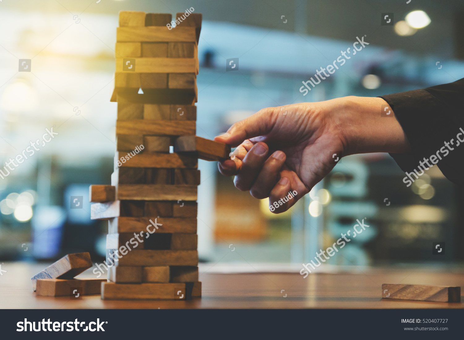 Hand of businessman pulling out or placing wood block on the tower in modern office.