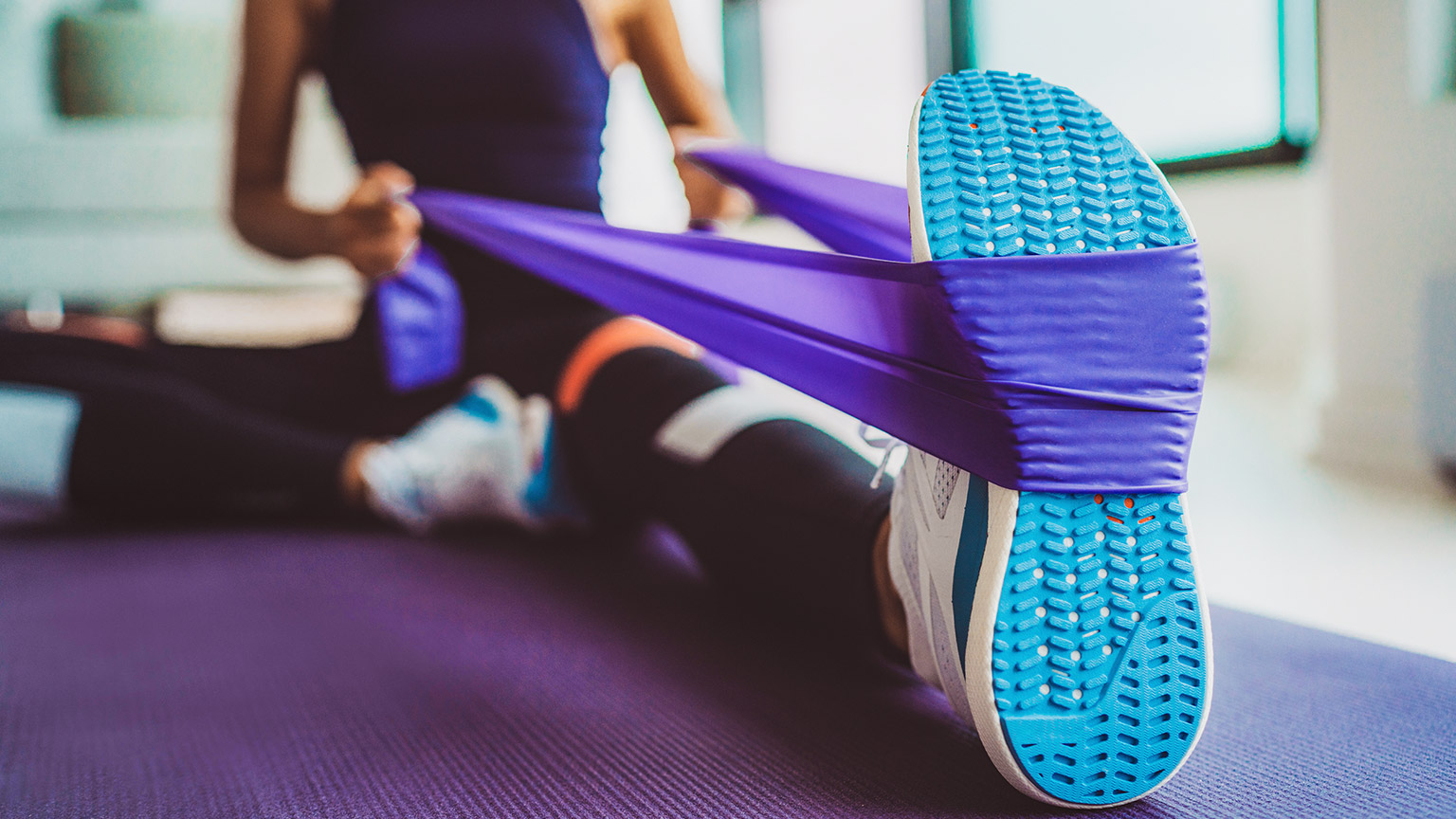 A woman sitting on the floor using a resistance band