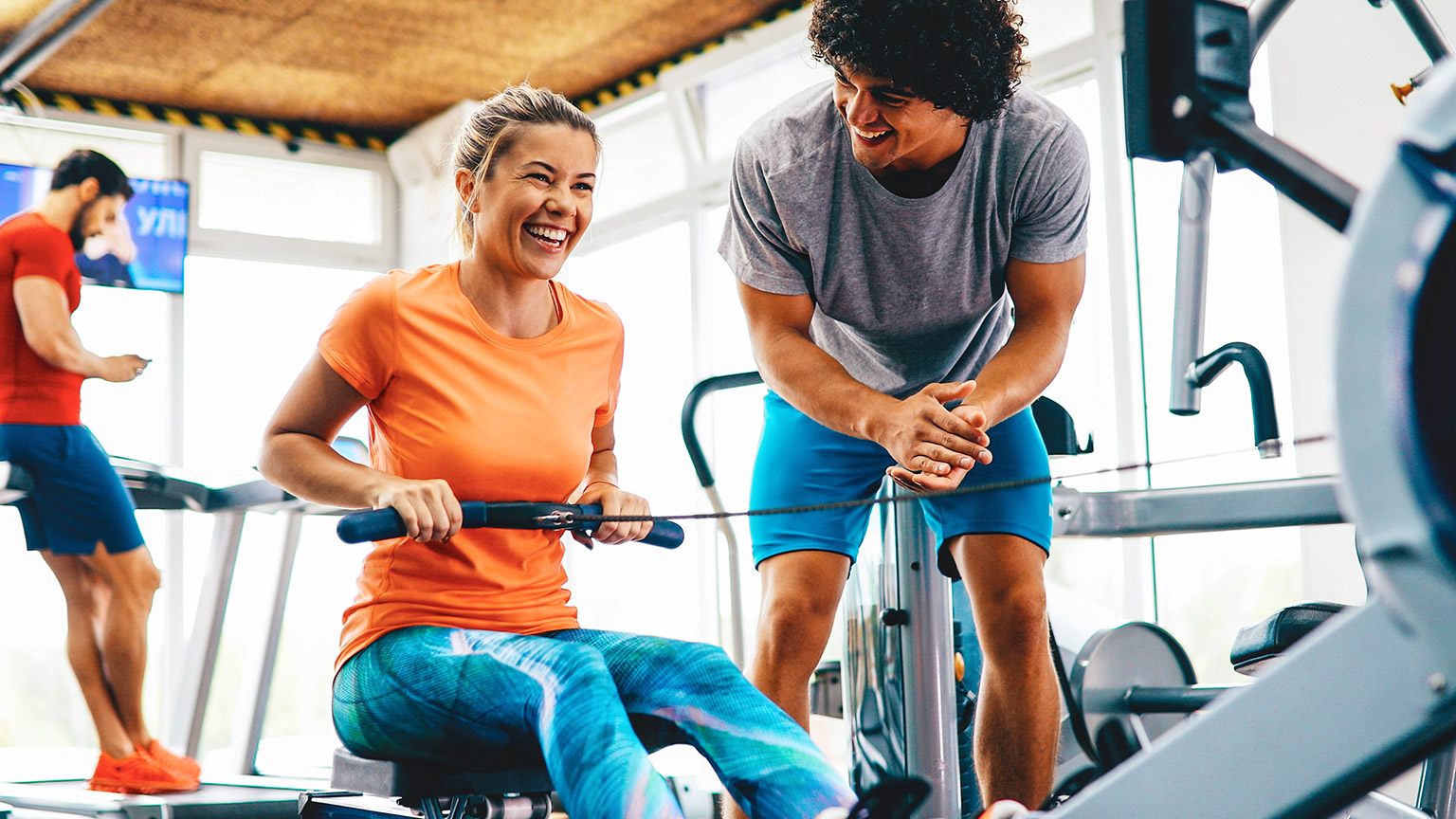 A personal trainer supporting a client using a rowing machine