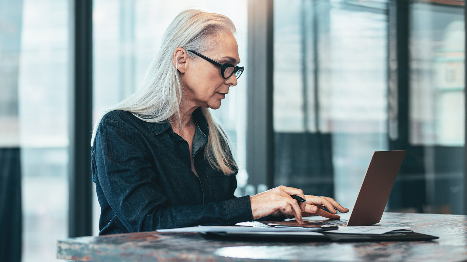 Businesswoman working at a desk on a laptop with business documents next to her