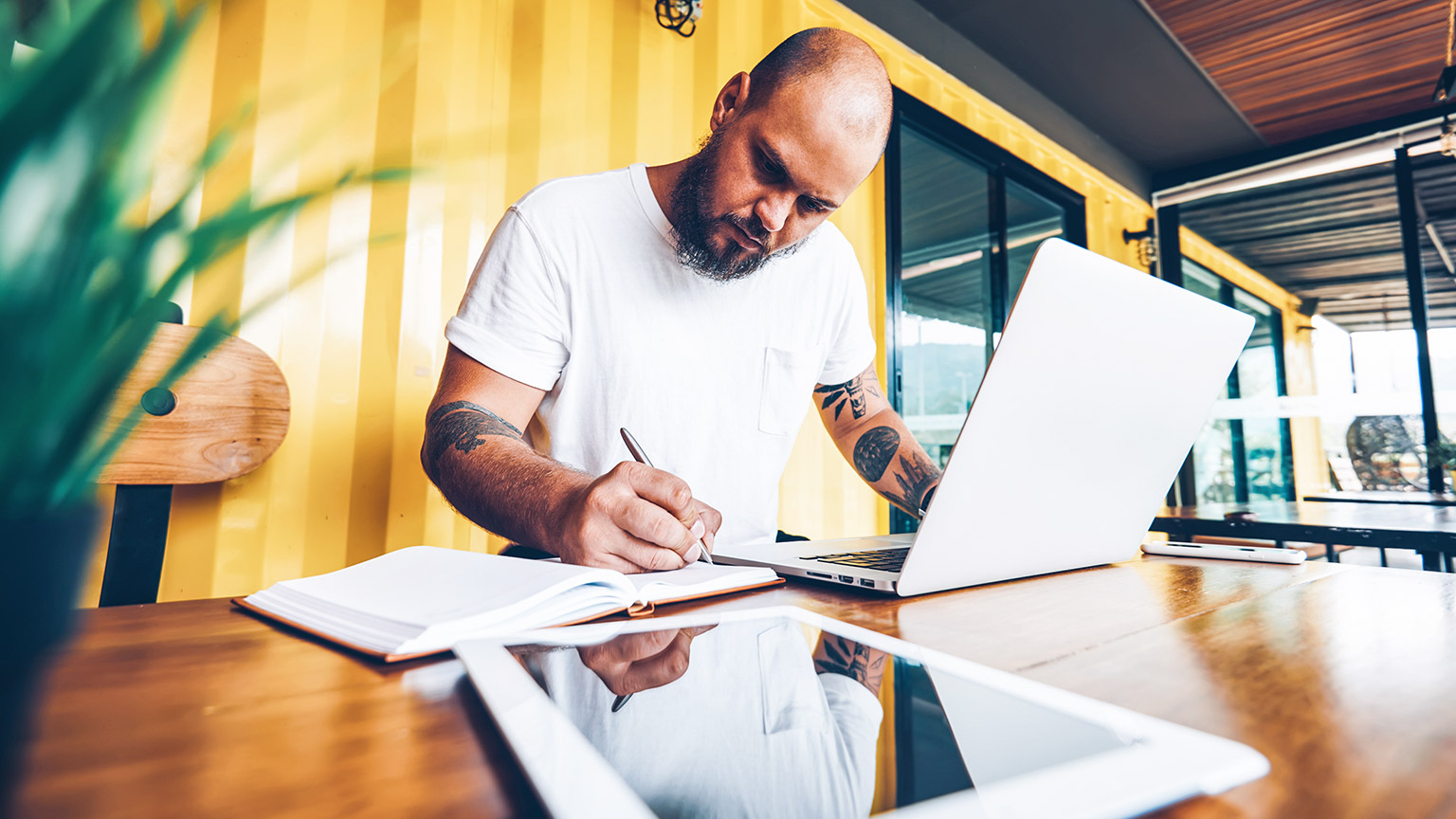 Bald man with notebook and laptop concentrating on paperwork 