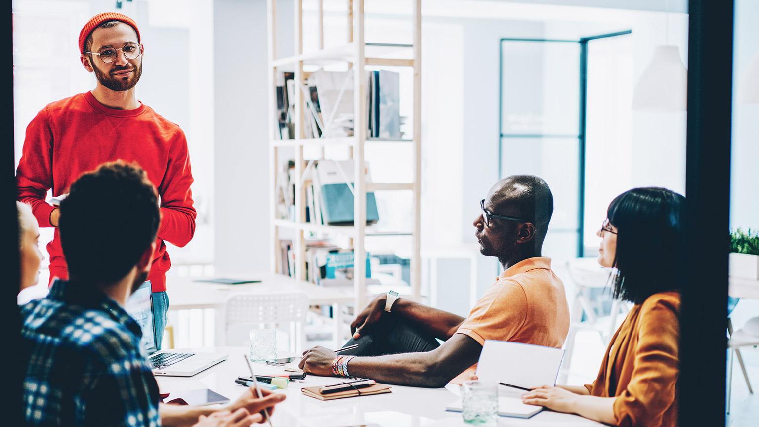 Male hipster presenting a design idea to colleagues who are seated at a table