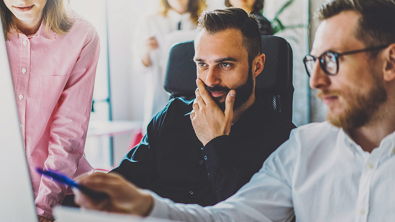 3 coworkers sitting at a desk looking at a computer while discussing a project