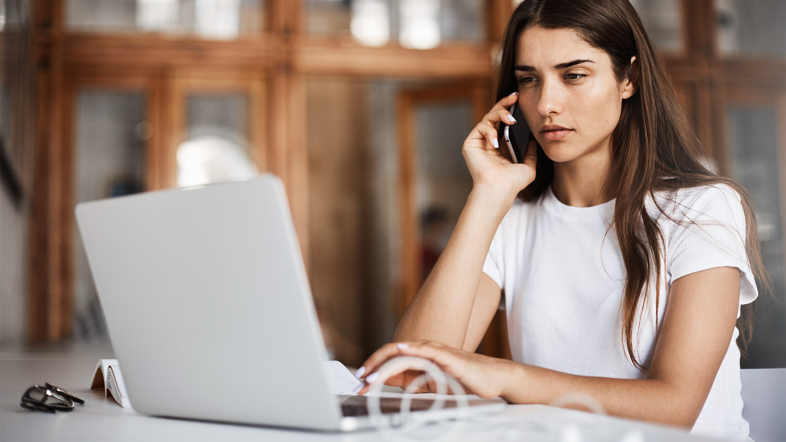 A professional seated at their desk in front of their laptop, while taking a call on their mobile