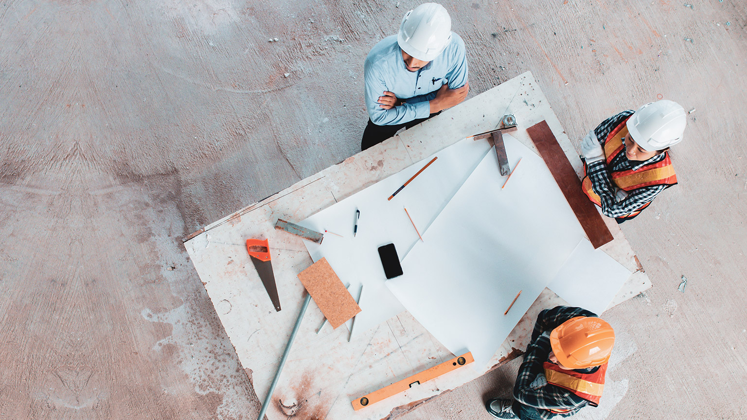 Top down view of 3 people standing around a table on a building site