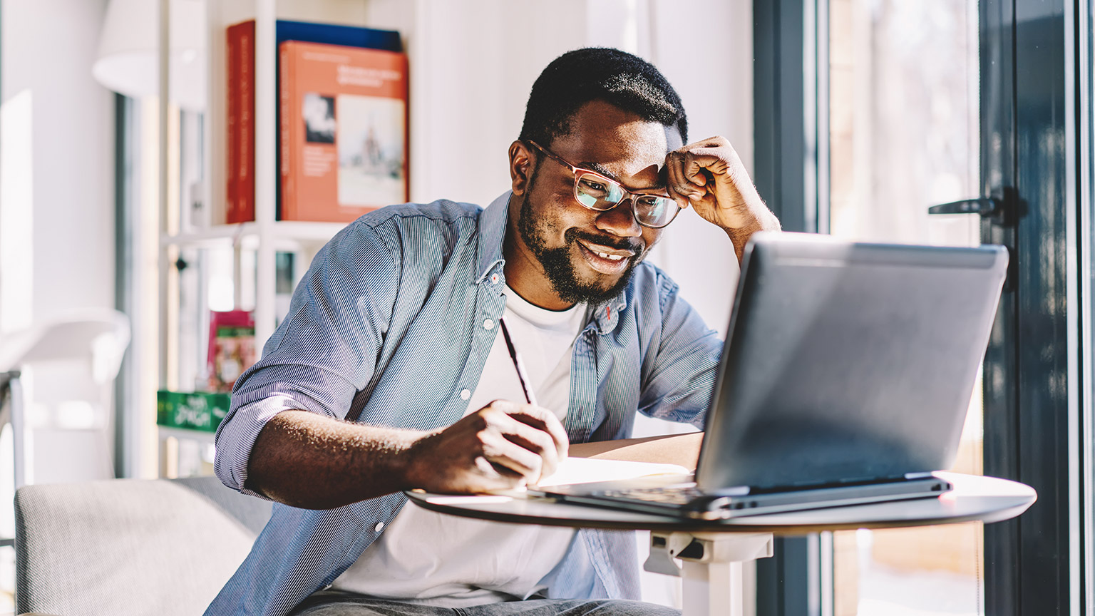 A person writing in front of a laptop