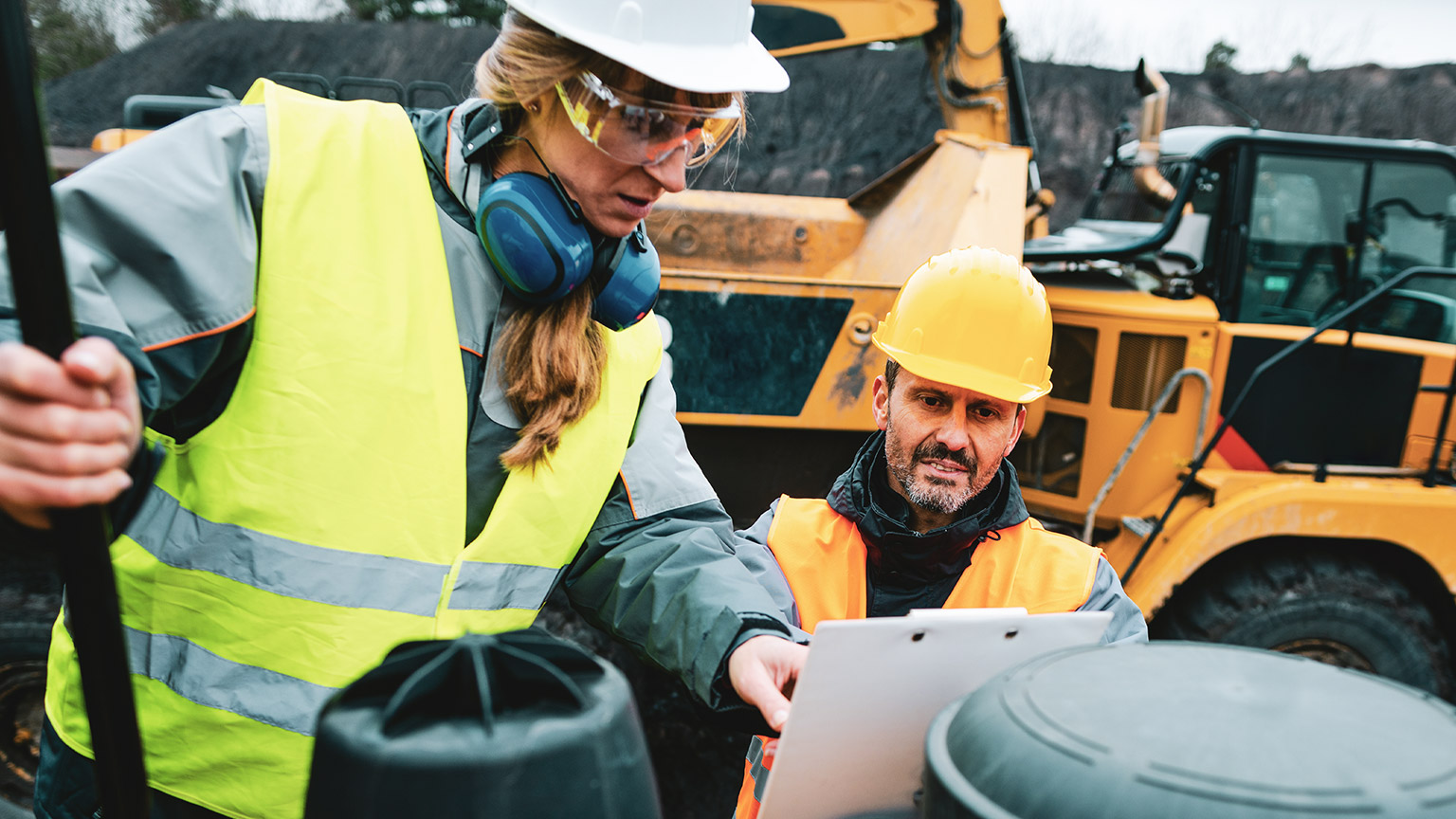 Male and female coworkers on a construction site looking at plans on a clipboard