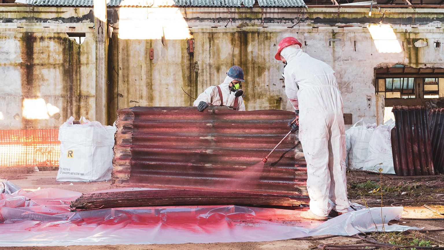 2 workers in hazmat suits disposing of asbestos roofing materials