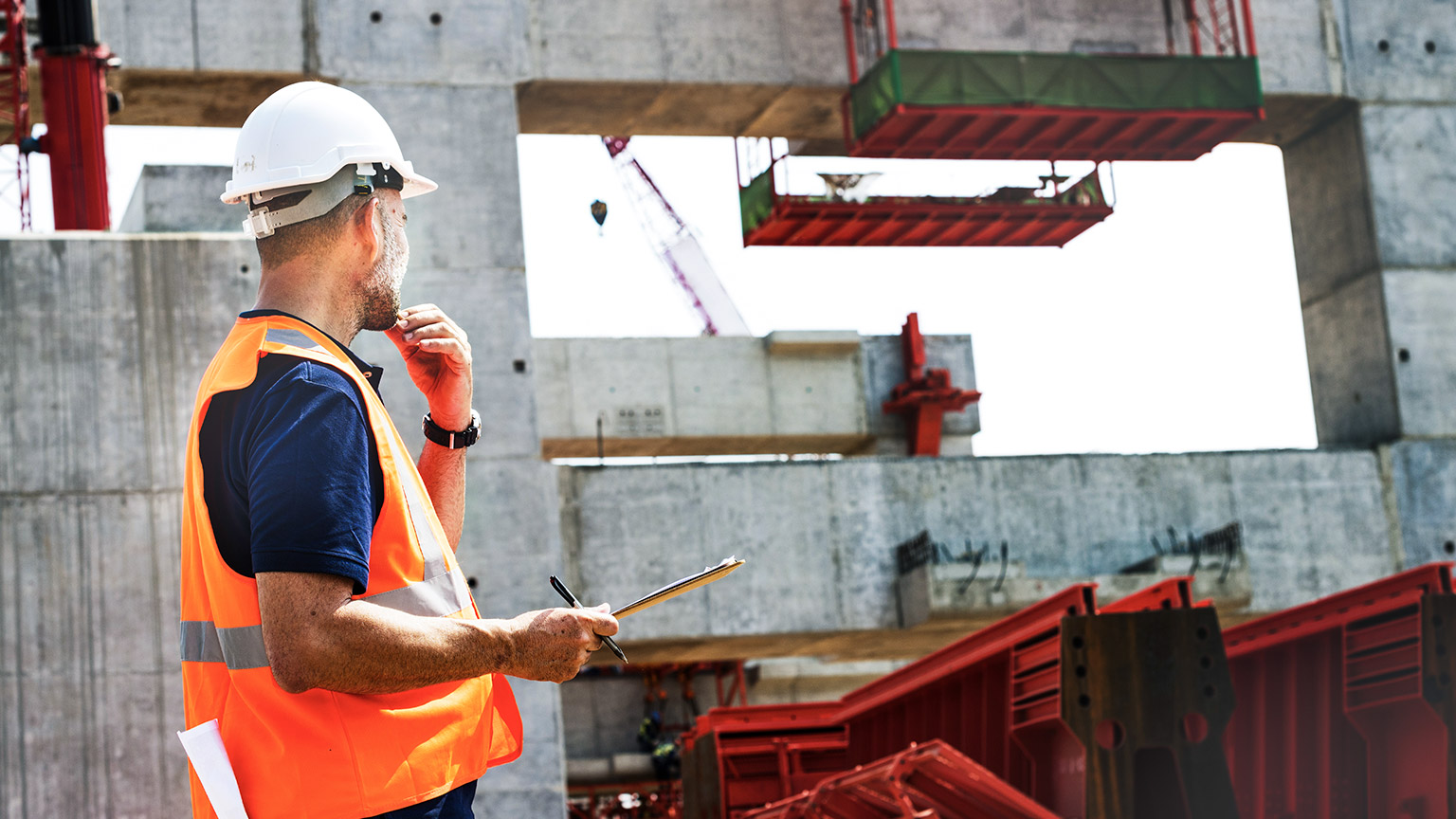 Supervisor on worksite wearing hi-vis and hard hat and carrying a clipboard