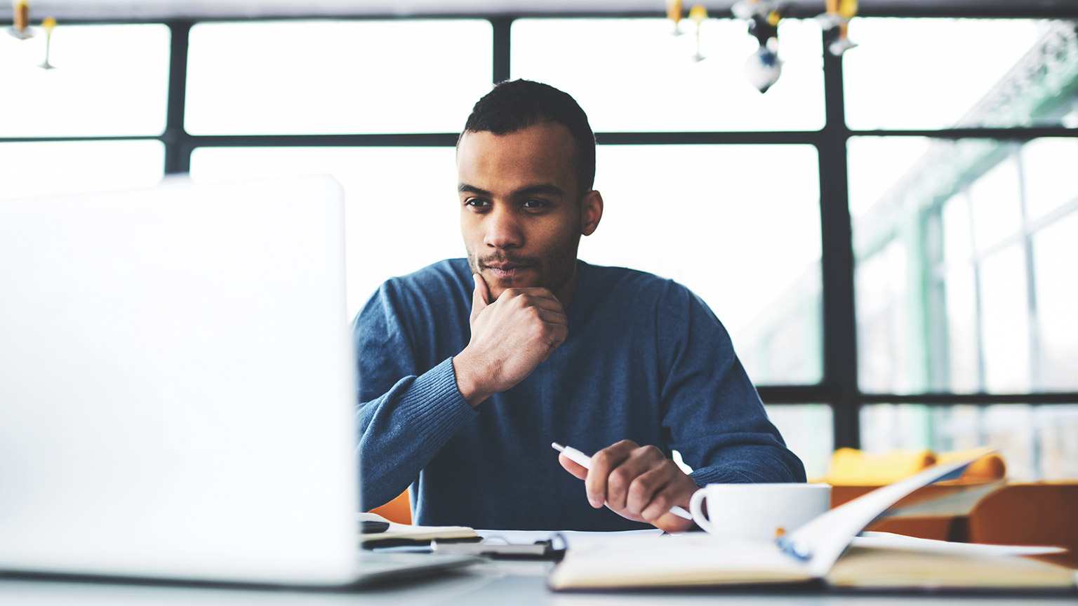 A young professional sitting in an open office reading construction-related legislation on their computer