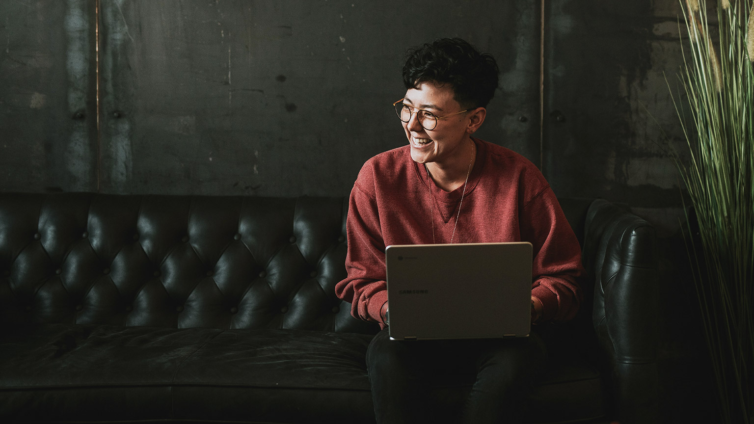 A young counsellor sitting on a couch with a laptop and a pleasant smile on their face