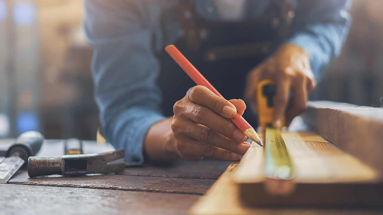 A close view of a carpenter using a pencil and tape measure to make a pice of wood before cutting