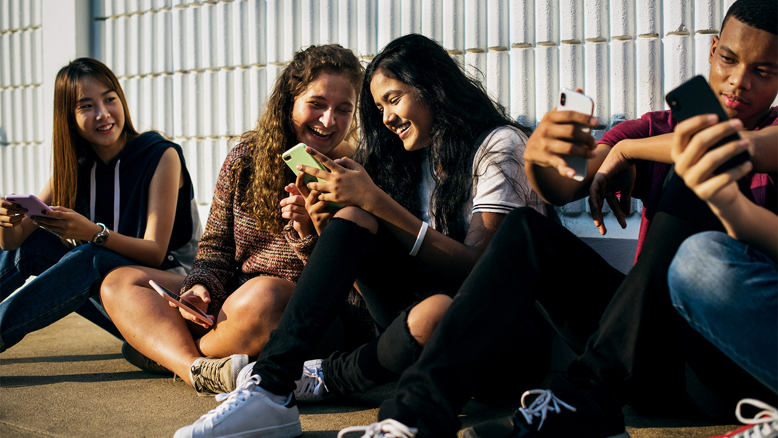 Group of young teenager friends laughing together using their phones