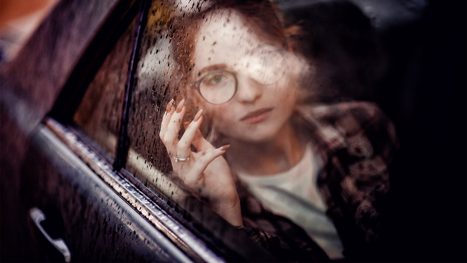 A young person looking solemnly out the passenger seat window of a moving vehicle