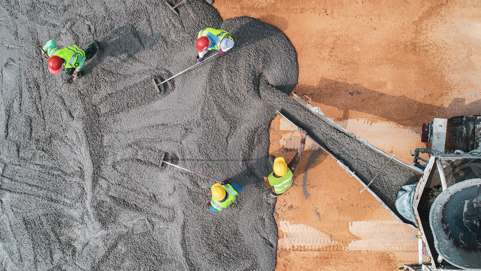 An aerial view of a group of concreters spreading newly poured cement on a building site