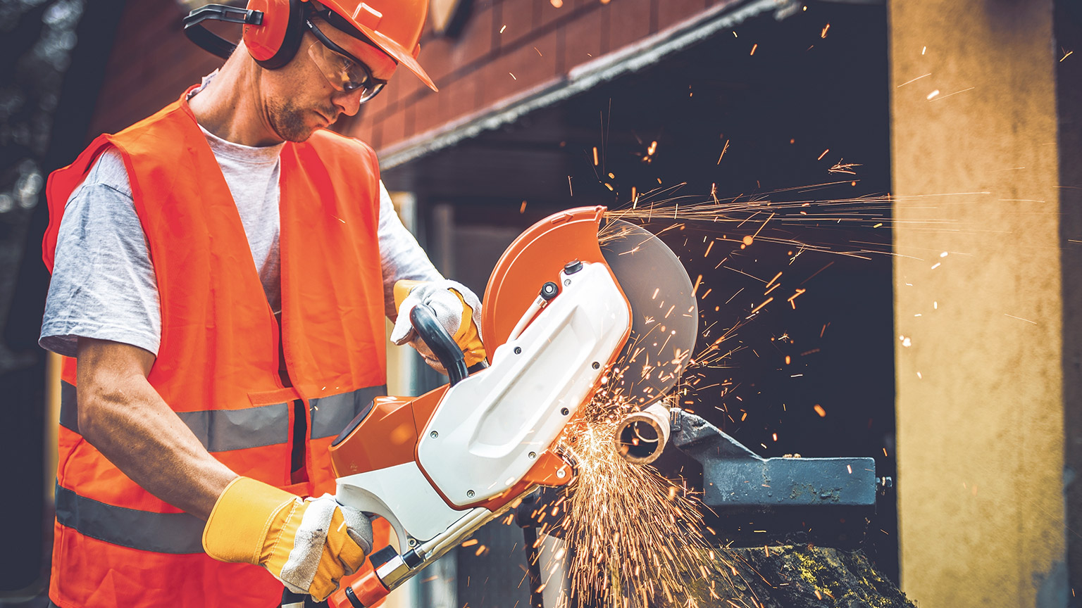 A construction worker using an angle grinder to cut a pipe on a construction site