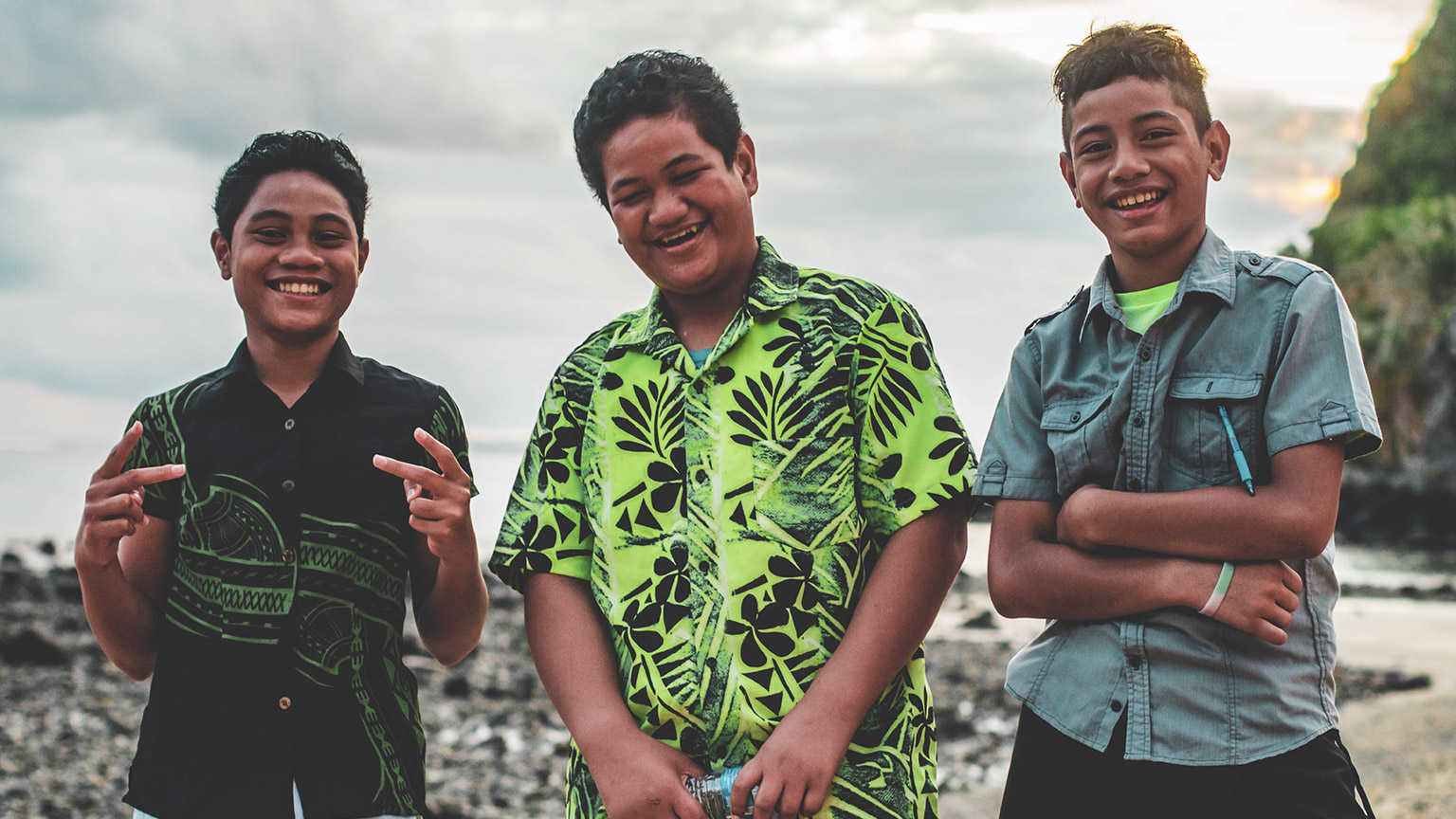 3 young pasifika youths smiling at the camera in the outdoors