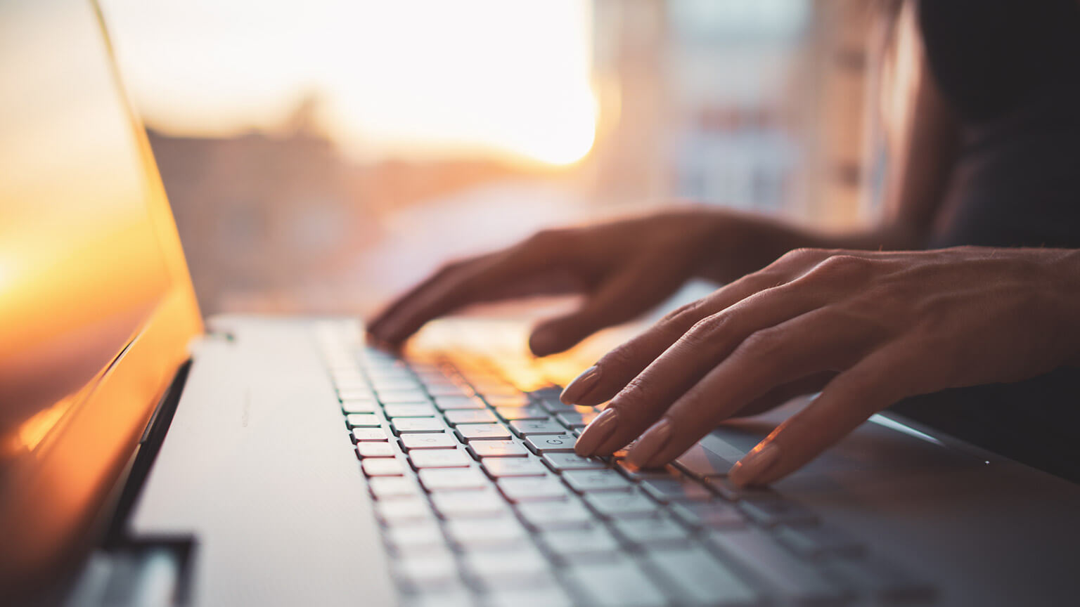 A close view of a business owner typing a laptop keyboard with the setting sun shining through the window