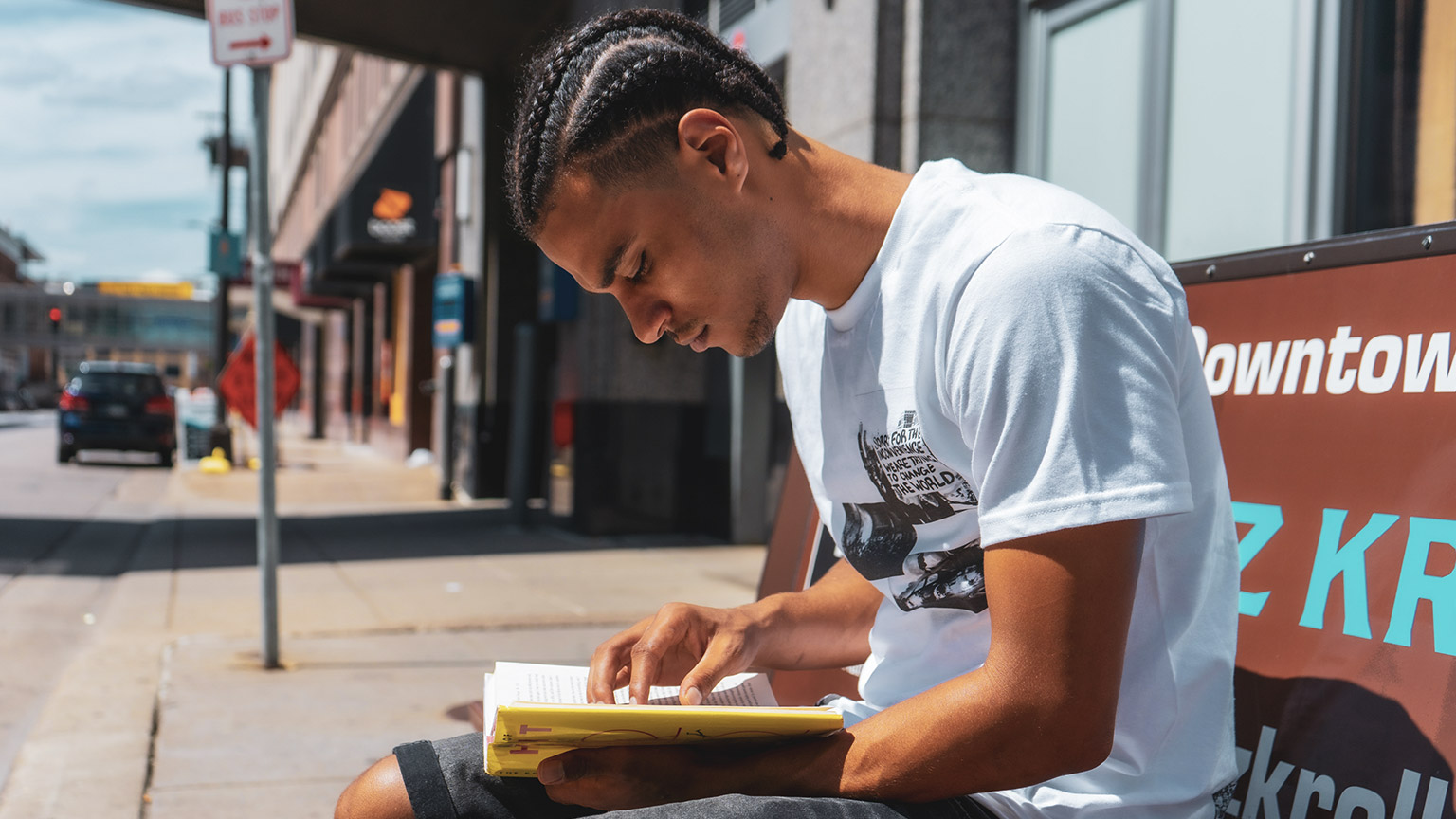 A youth sitting outside on a bench reading a book