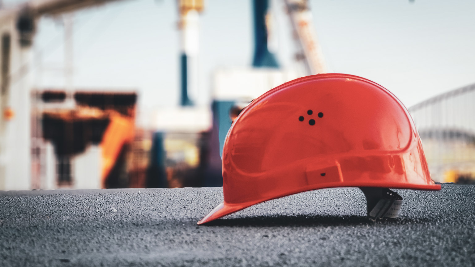 A single red construction hard hat sits on a rough surface on a building site