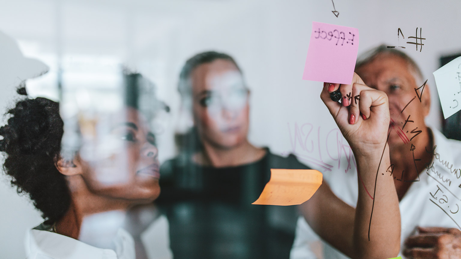 3 colleagues writing project notes on a glass window