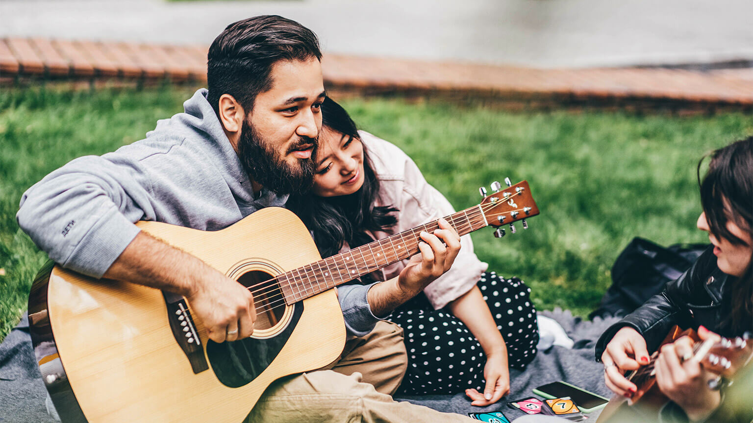 Teenagers sitting outside, playing card games and strumming a guitar