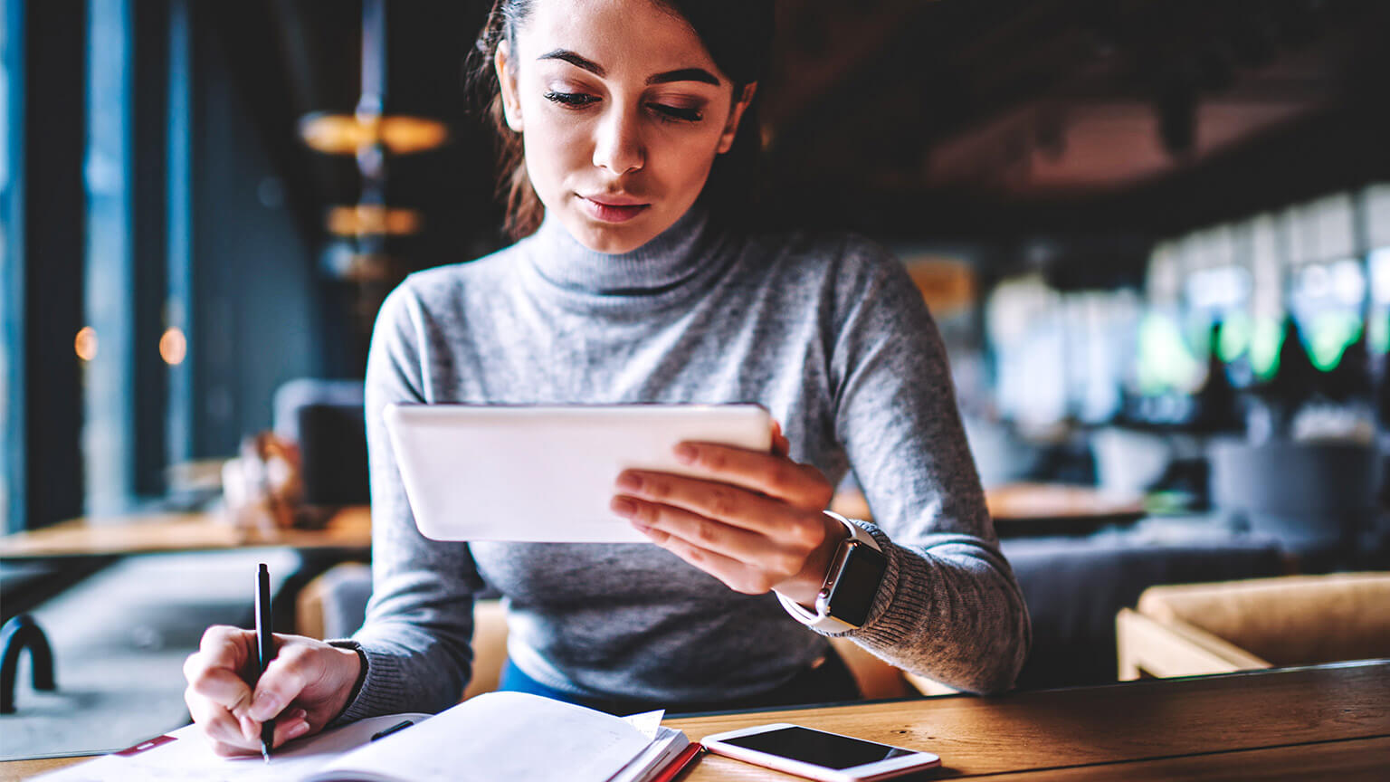 A professional, referencing their tablet while taking down some hand-written notes in their journal