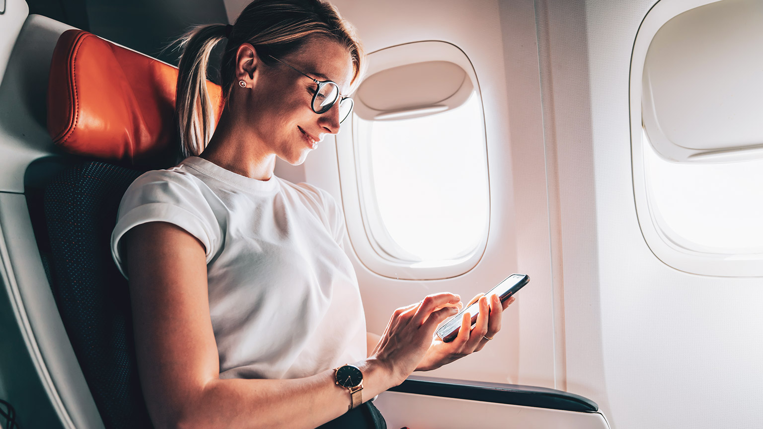 A entrepreneur sitting in business class on an aircraft looking at her mobile phone