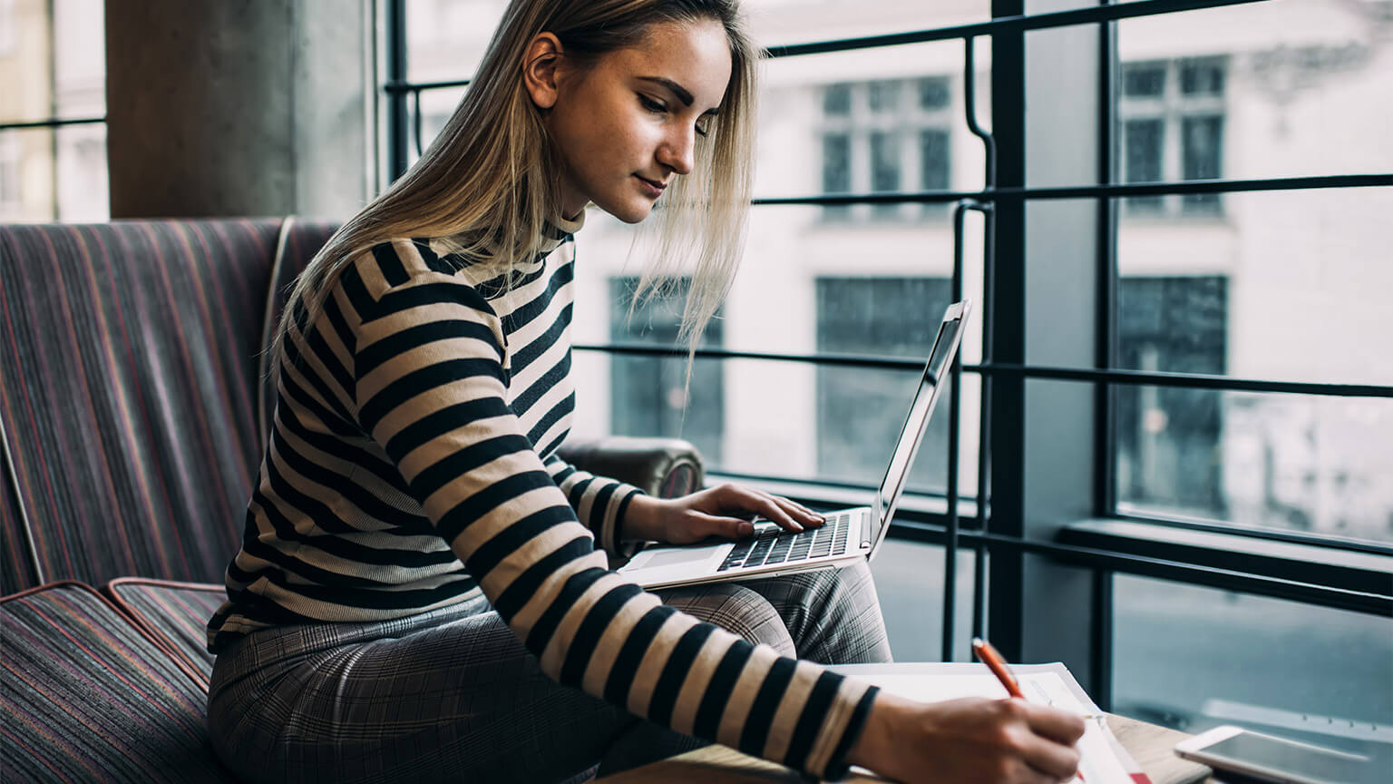 A student taking down notes from an online resource found on their laptop