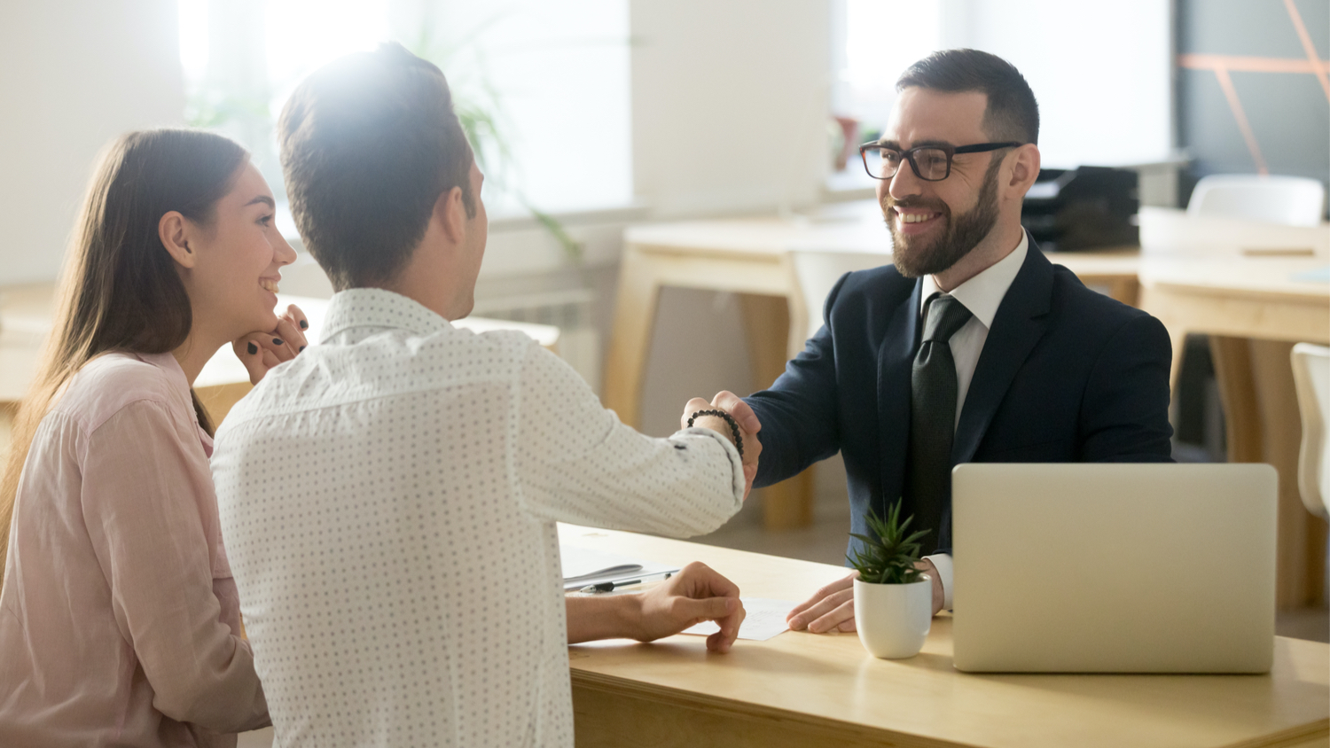 Smiling lawyer, realtor or financial advisor handshaking young couple thanking for advice.