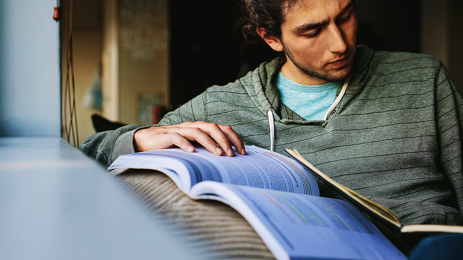 A person studying reference material intently, by their window