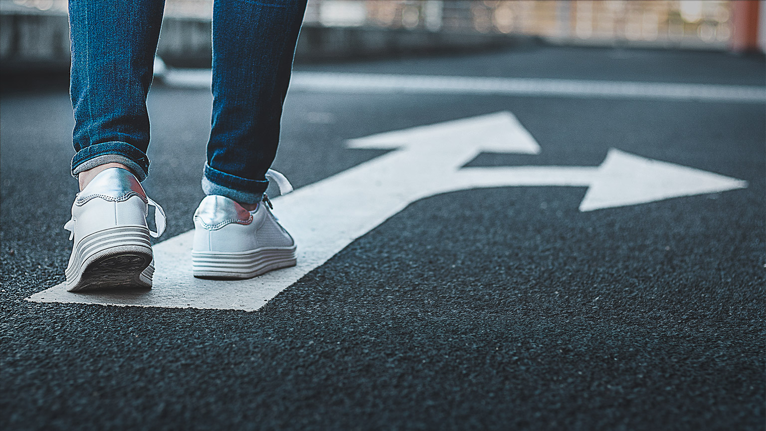 A person walking along a quiet street, approaching a fork in the road