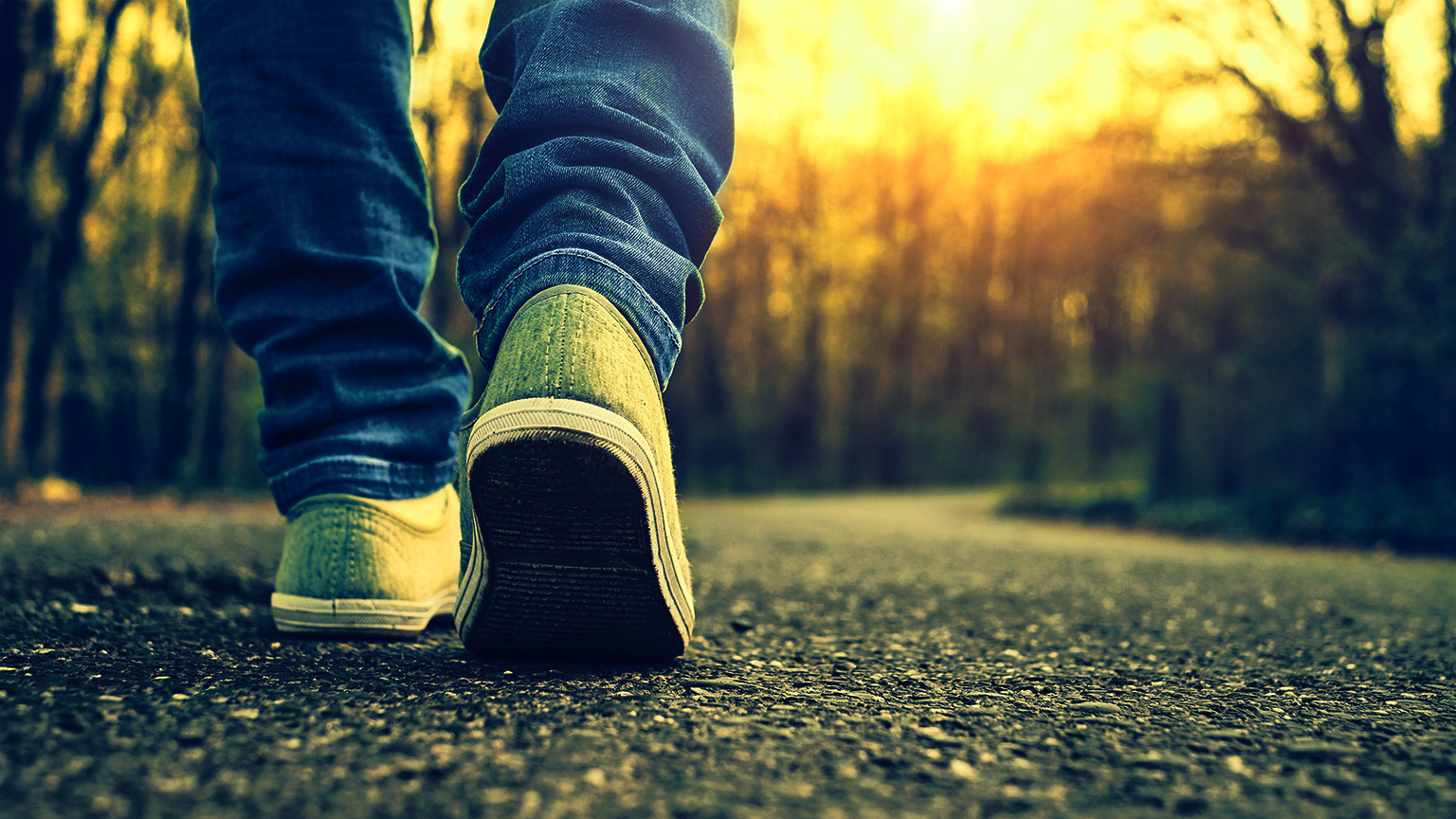 A person mid-stride, walking on the side of a quite road