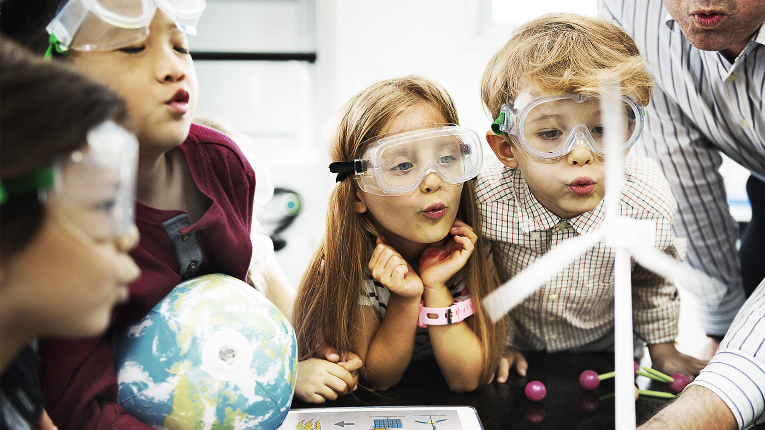 Children blowing on a miniature wind turbine during a class