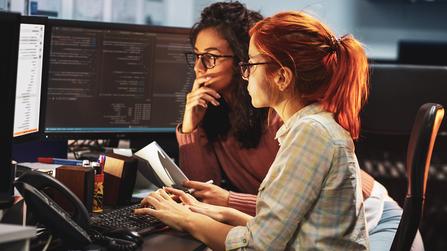 A pair of programmers in an office working on a desktop computer