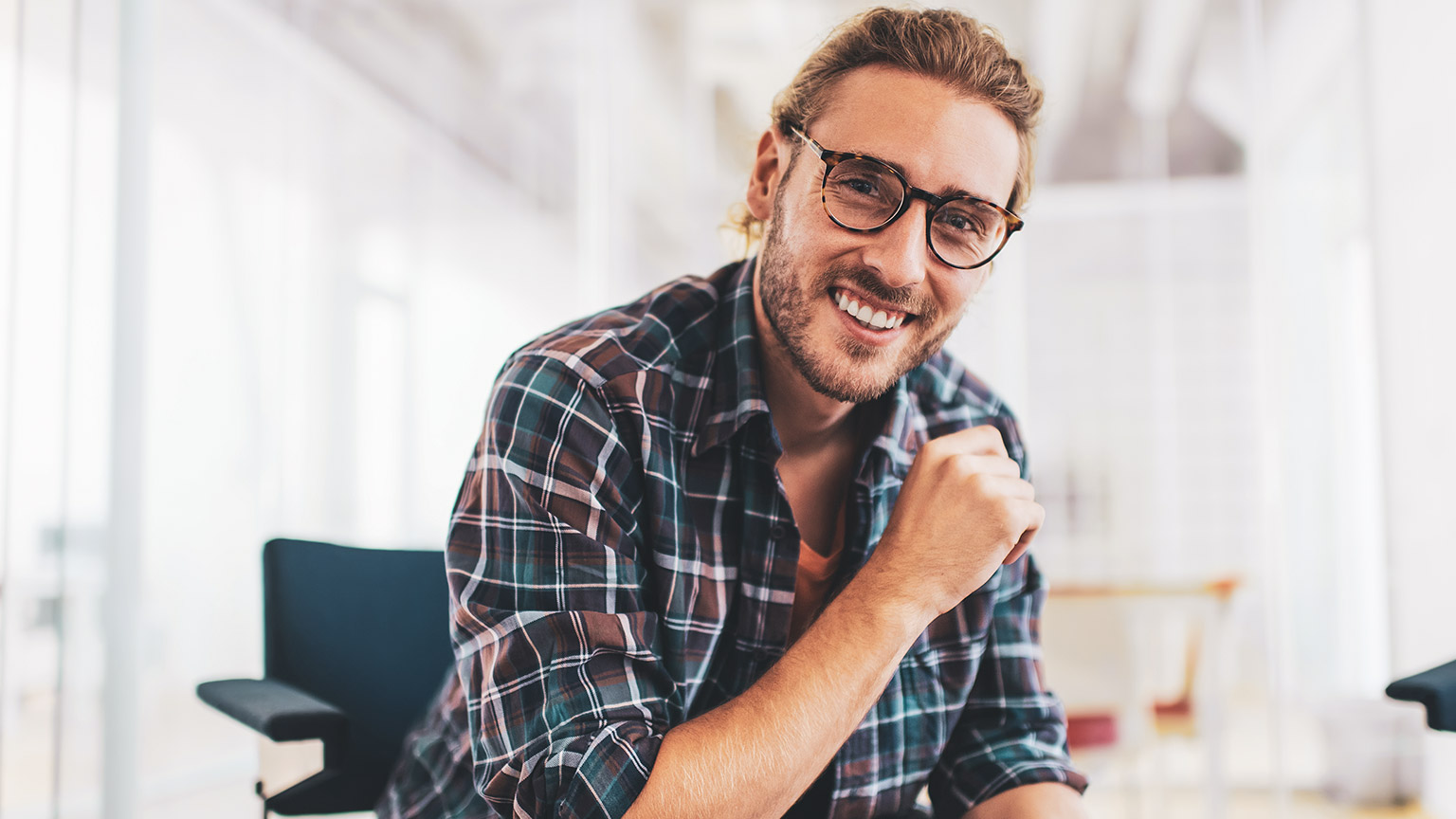 A young business manager smiling at the camera, while sitting in a relaxed office environment