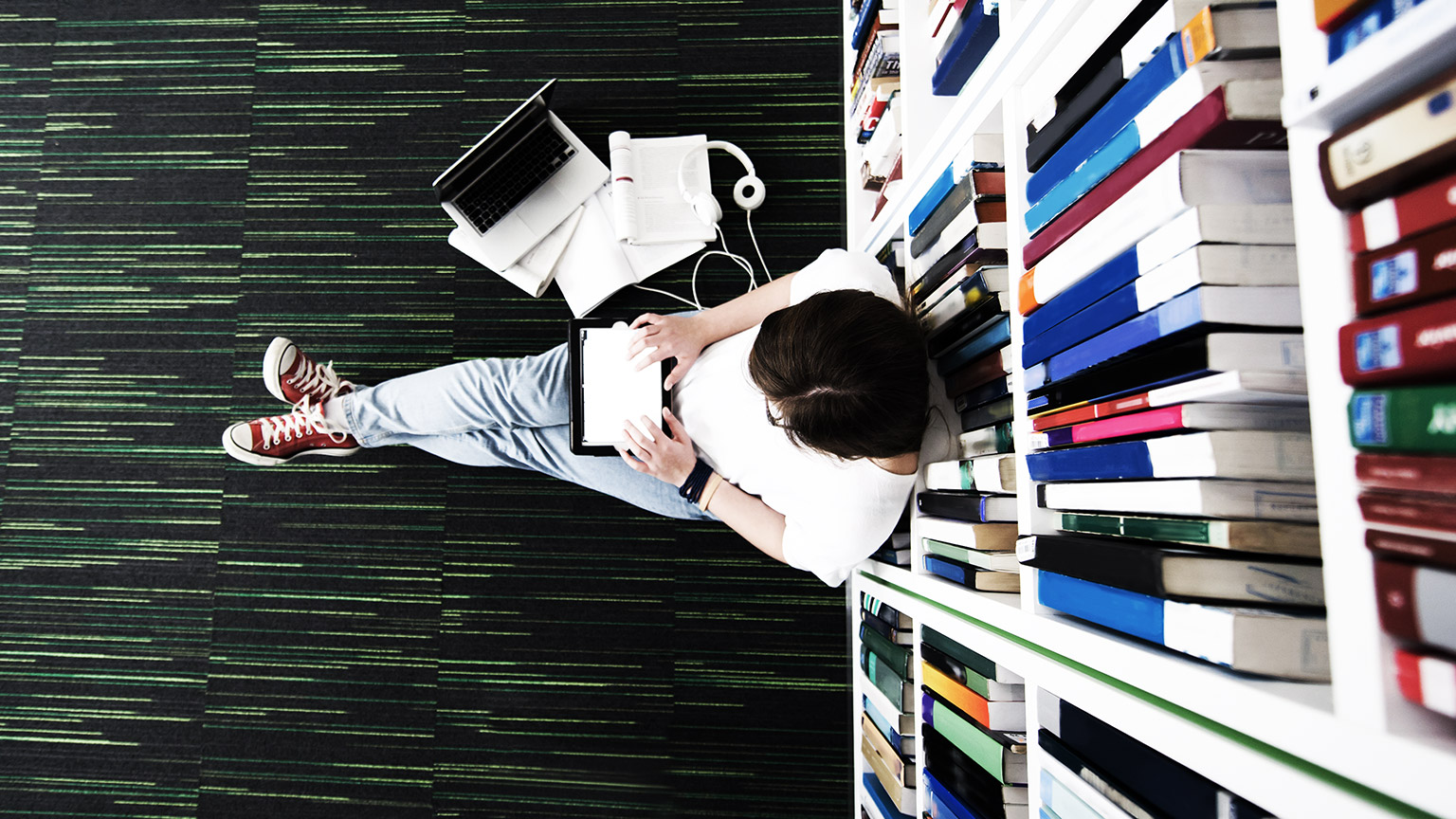 A student sitting on a library floor, absorbing resources relating to their latest project