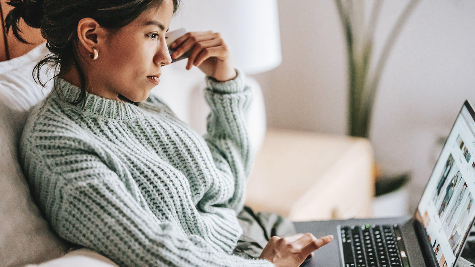 A young person sitting on a couch surfing the web on a laptop