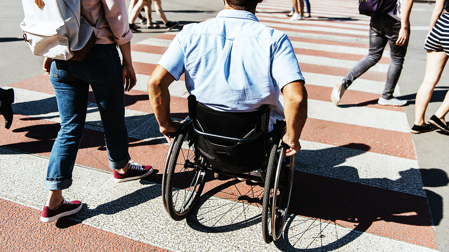 A carer and their client crossing the road at a busy intersection