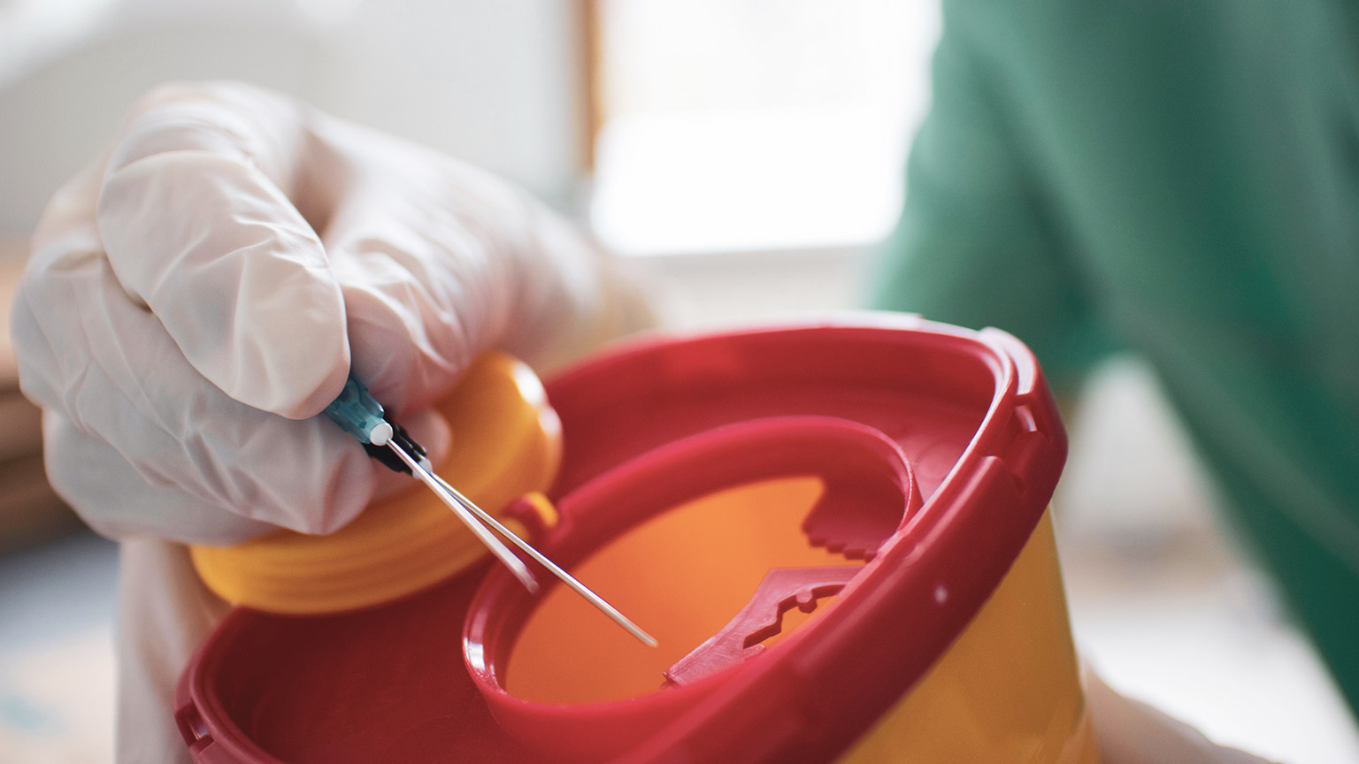 A close view of a person disposing of a needle in a sharps container