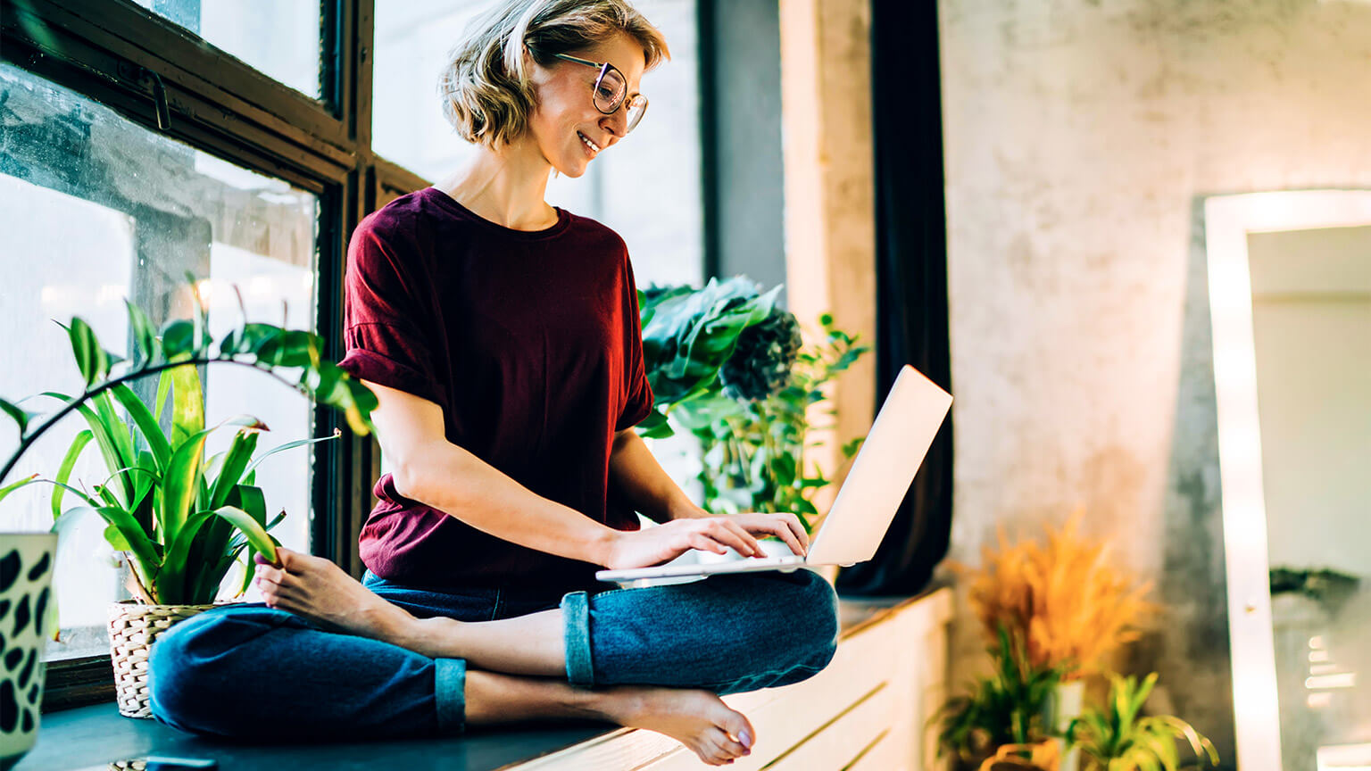 A student perched on a bench in their home, making notes on their reference material