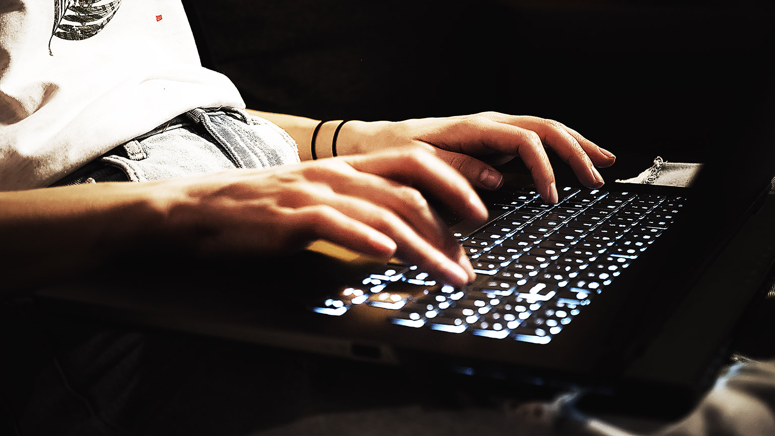 A close up of a programmerr using laptop working from home with a backlit keyboard