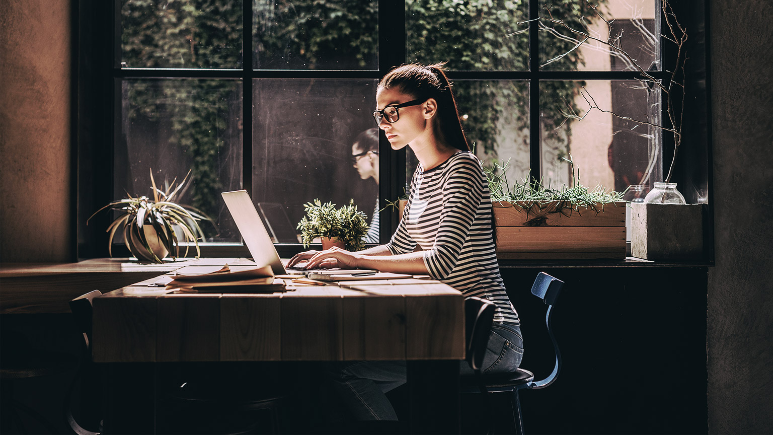 A person in smart casual wear working on laptop while sitting near window.