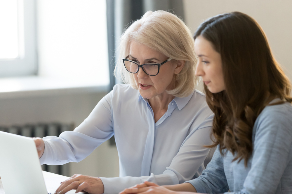 ID: 1332825533  Serious old female mentor teacher coach teaching intern or student computer work pointing at laptop