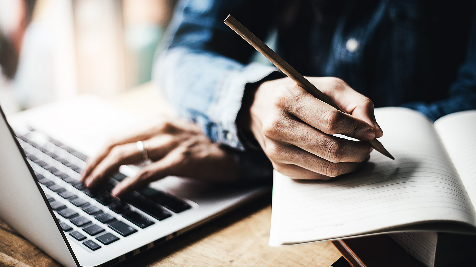 A person writing notes while researching on a laptop online