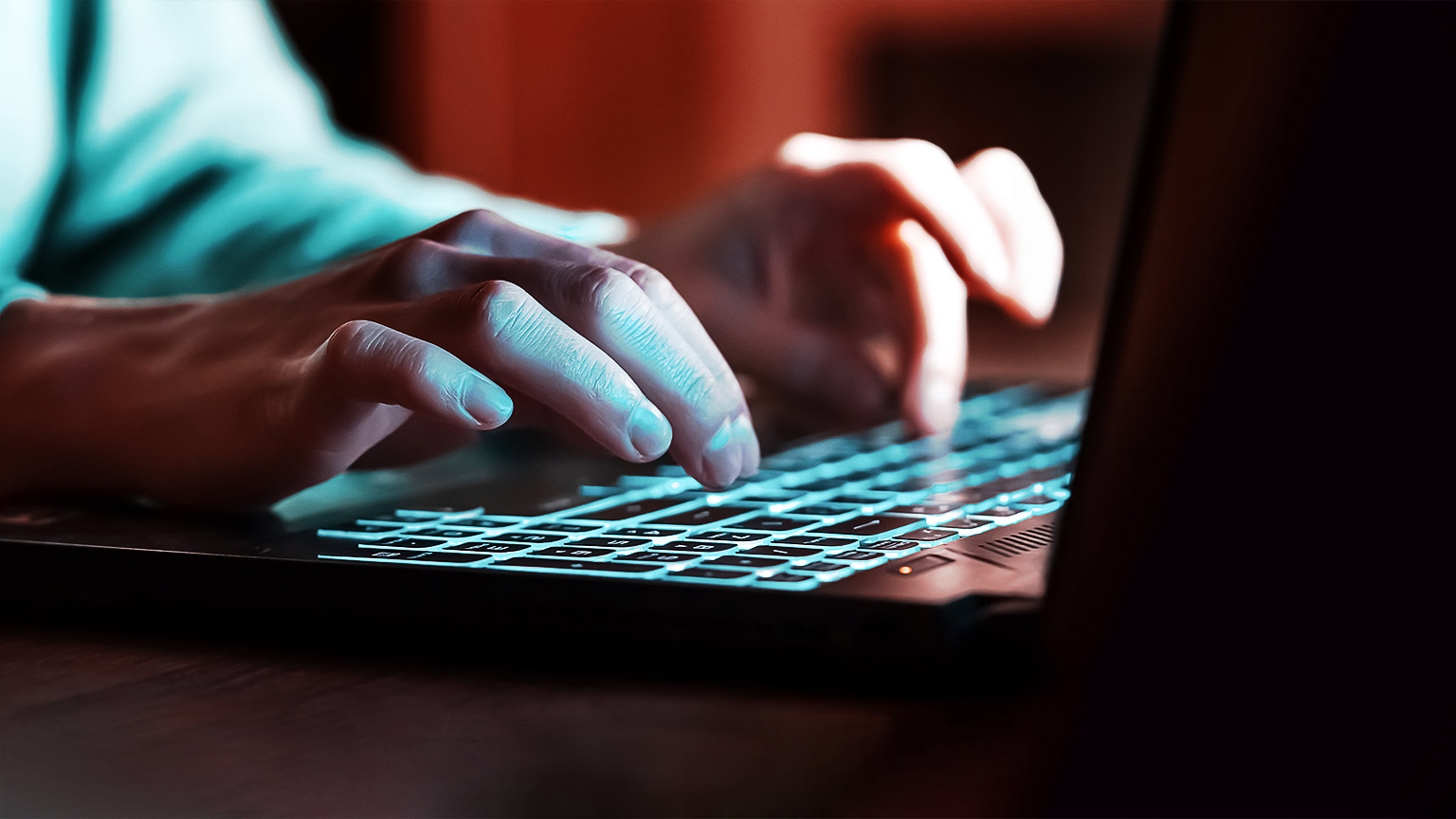 A person typing in a dark lit room