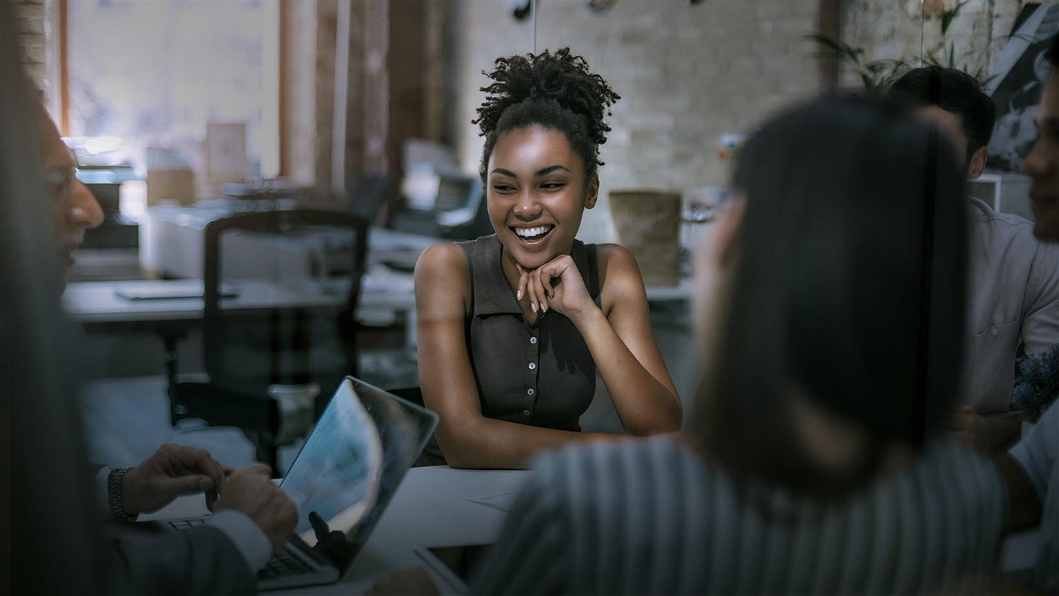 Young and cheerful Afro American woman smiling while having a meeting with colleagues in the modern office