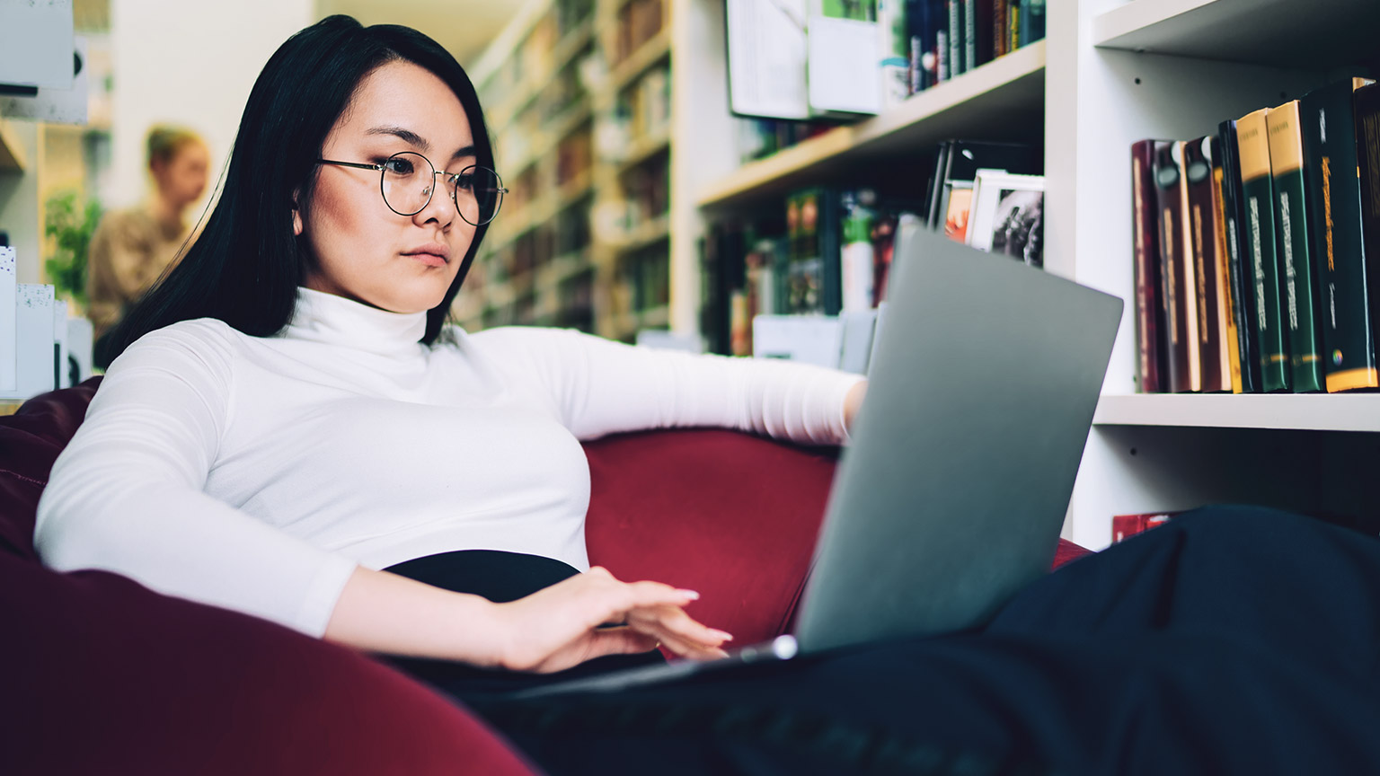 A student sitting in a comfy chair in a library reading online resources